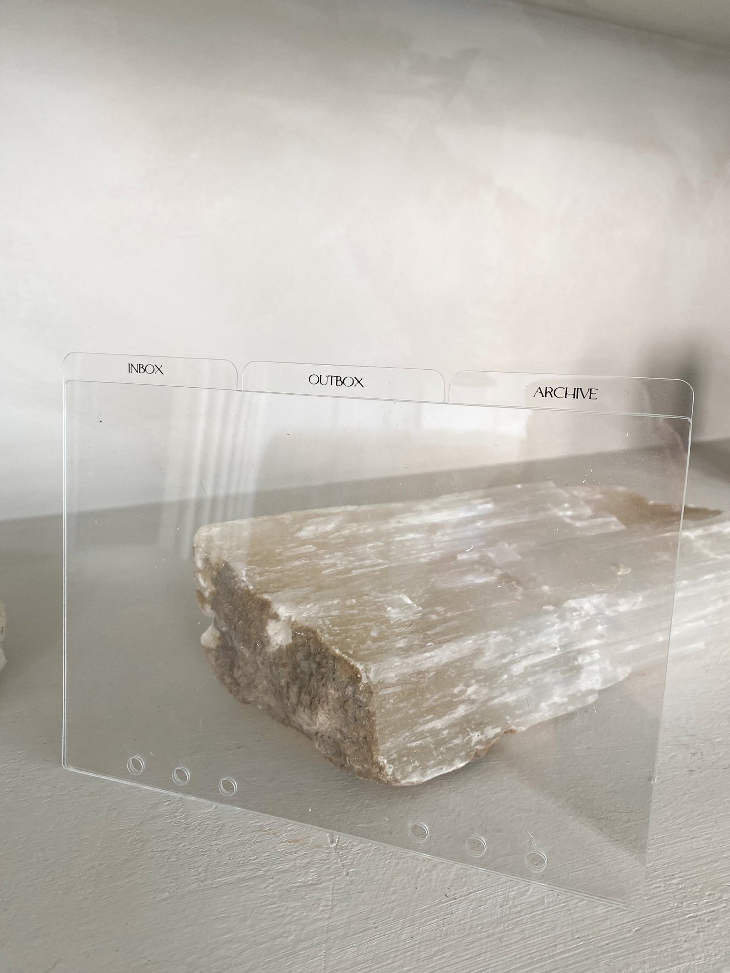 IOA acrylic divider propped up by a crystal, showcasing its transparent nature and elegant design, with tabs labeled 'Inbox,' 'Outbox,' and 'Archive.